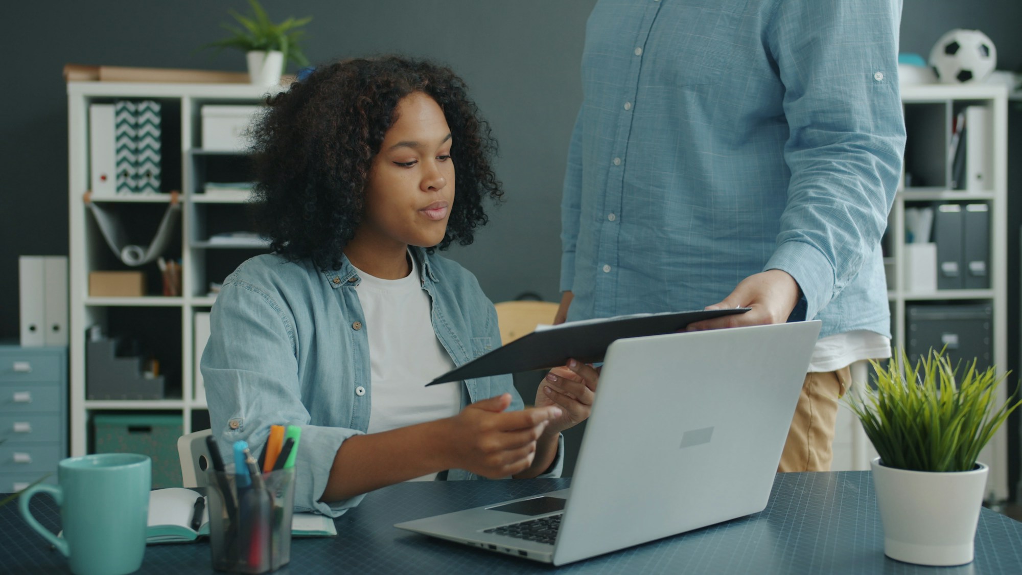Two colleagues reviewing a folder of documents beside a laptop in an office