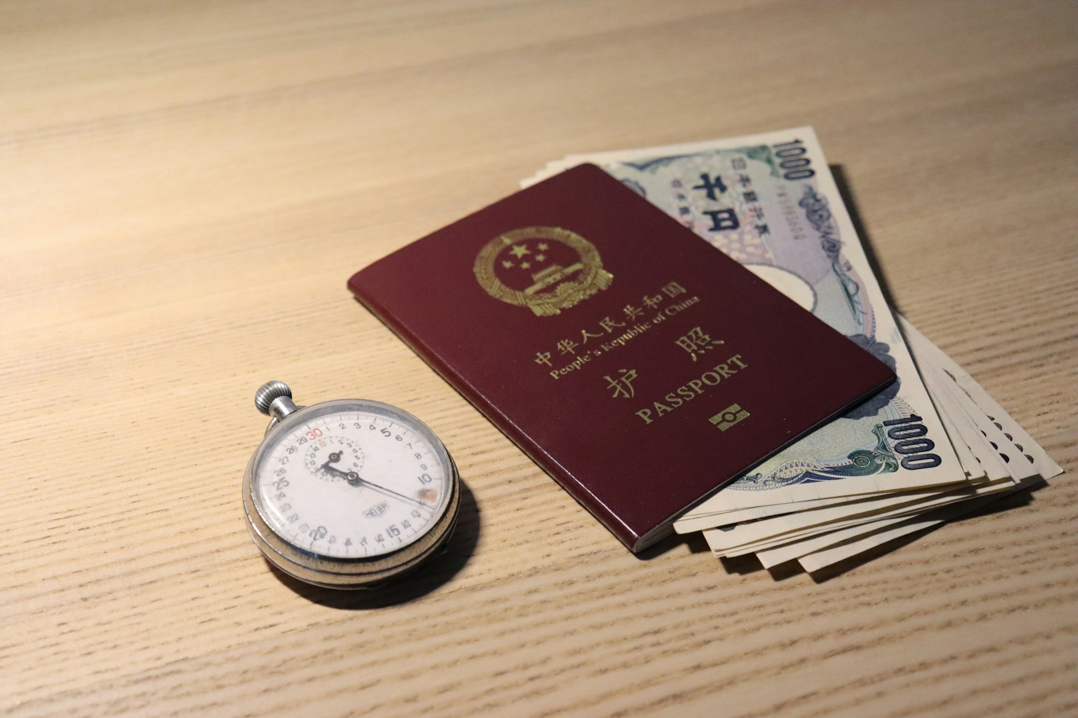 Chinese passport on a desk beside travel papers and a stopwatch